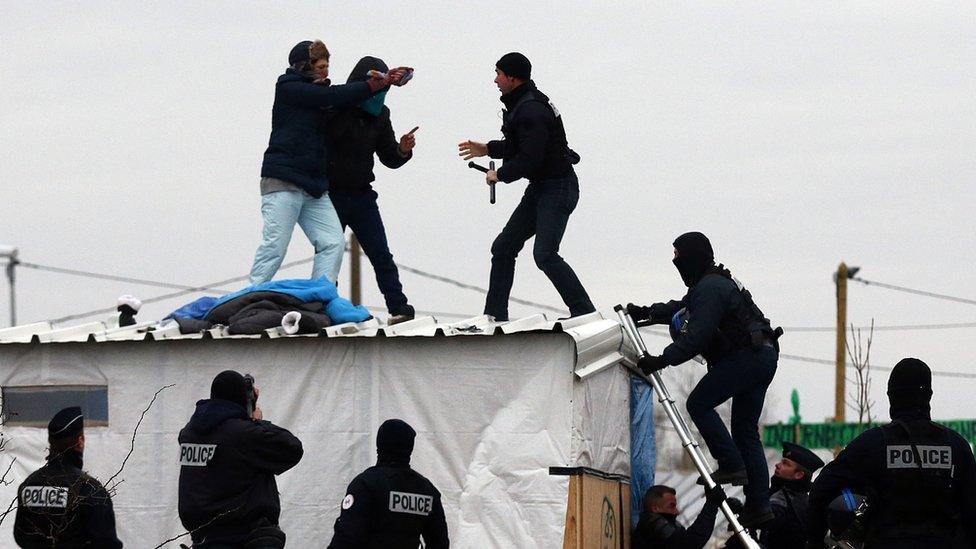 A woman threatens to cut her wrist with a knife as French police remove her and a man from the top of a hut as they clear the "jungle" migrant camp on March 01, 2016 in Calais, France.