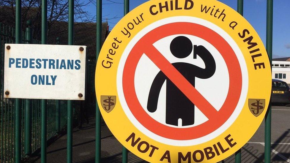 A sign at the school gates, which says: "Greet your child with a smile not a mobile"