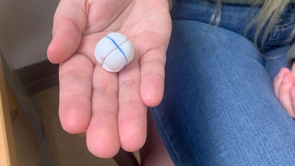 A close-up image of the RefluxStop implant - a small white circular ball - on Danielle Harding's hand