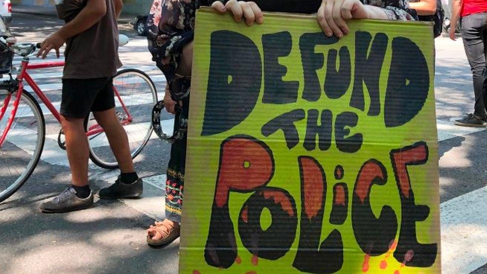 Woman holds protest sign which read defund the police.