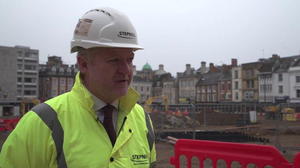 Man in hi-viz jacket and helmet stands in front of town centre building site