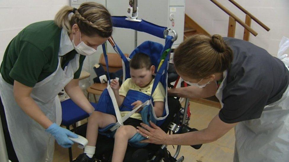 Two female nurses attend to a young boy in a lifting hoist