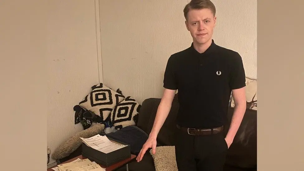 Harvey Benson, who is wearing a black t-shirt and trousers, stands next to files of paperwork