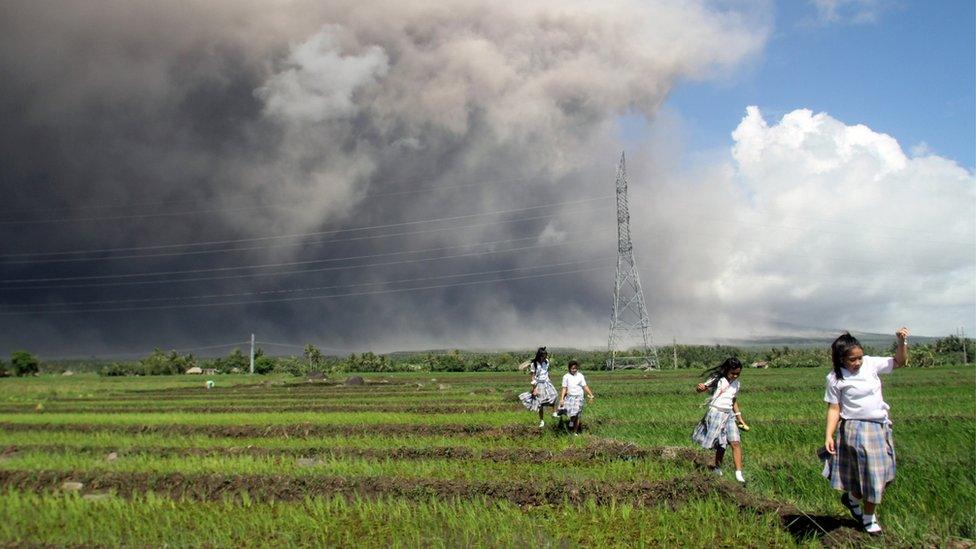 Students passes through the rice paddy as they run away from cascading volcanic materials from the slopes of Mayon Volcano in Guinobatan, Albay province, south of Metro Manila, Philippines