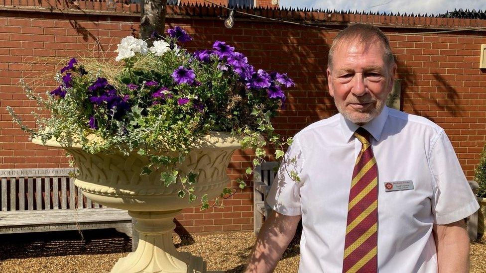 Man in cricket club tie stands next to a stone plinth