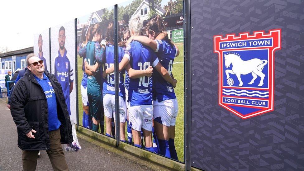 A fan walking into Portman Road in front of an Ipswich Town Women's board