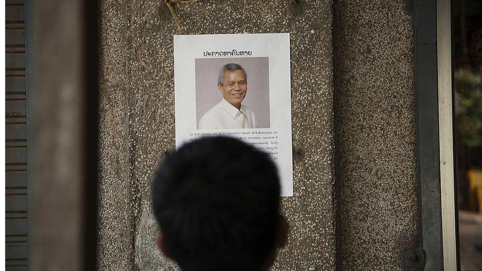 A local person reads a "missing person" poster for Sombath Somphone in Vientiane, Laos