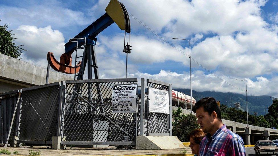 People walk by oil pump in Caracas on November 14, 2017