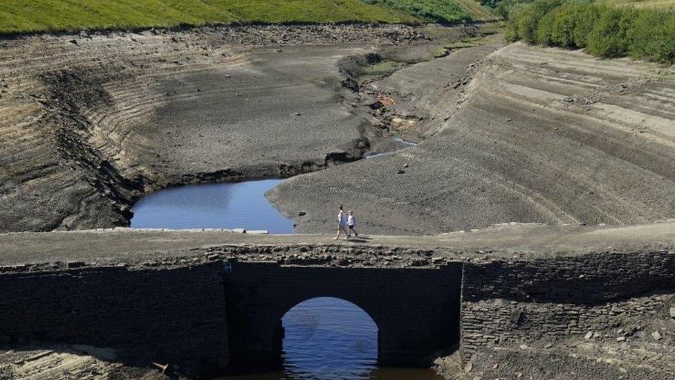 People walk across the dry cracked earth at Baitings Reservoir in Ripponden, West Yorkshire, where water levels are significantly low