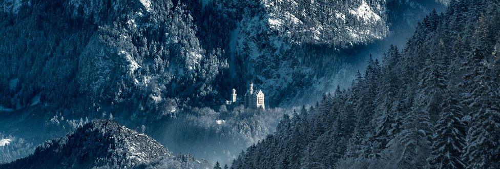 A snowy mountainous landscape with a castle perched on a hill