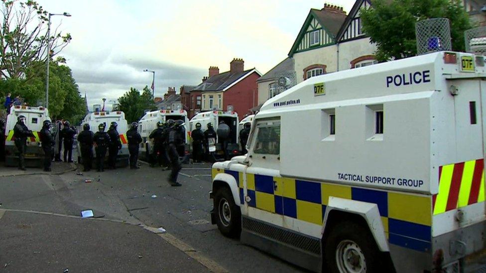 Police officers in riot gear standing behind police Land Rovers in north Belfast