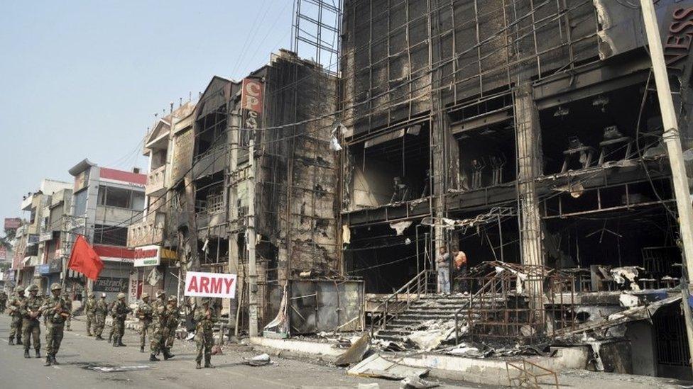 Indian soldiers conduct a flag march past damaged buildings at Rohtak (20 February 2016)