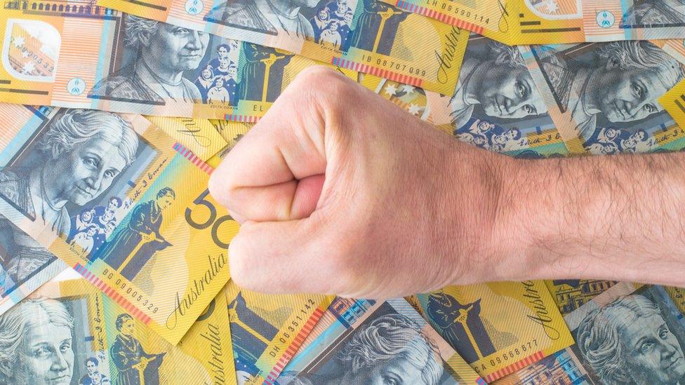 A fist rests on top of several Australian $50 notes