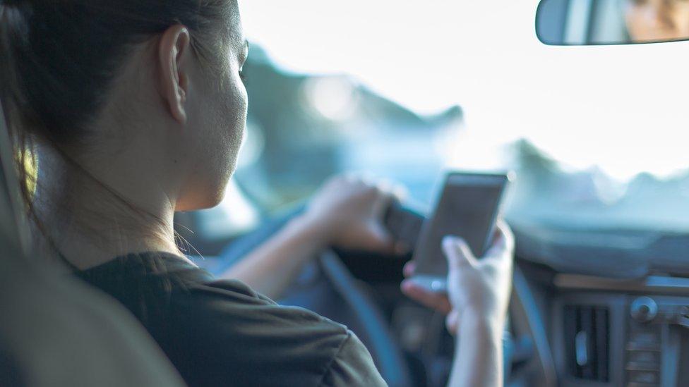 Stock image of a driver using a hand-held mobile at the wheel