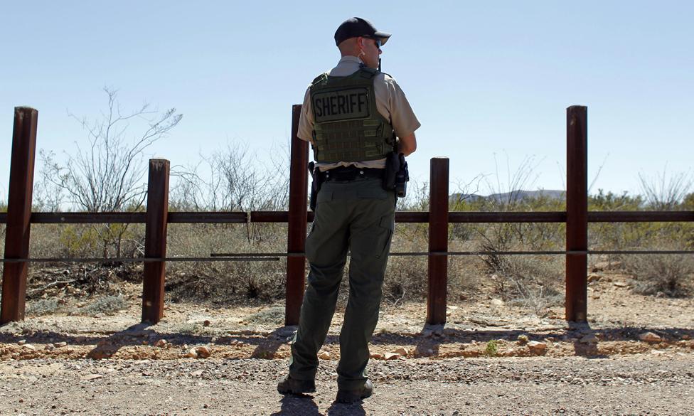 A Douglas County Sheriff"s Office deputy stands in front of the US border with Mexico while Republican presidential candidate Sen Ted Cruz visits the border with Mexico in Douglas, Arizona