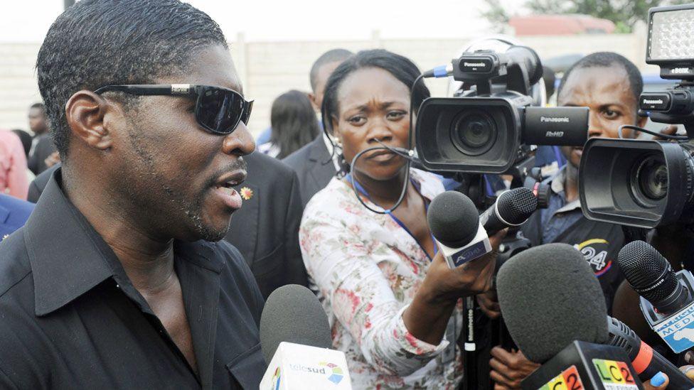 Teodoro Obiang Mangue wearing sunglasses talking to reporters who are holding microphones