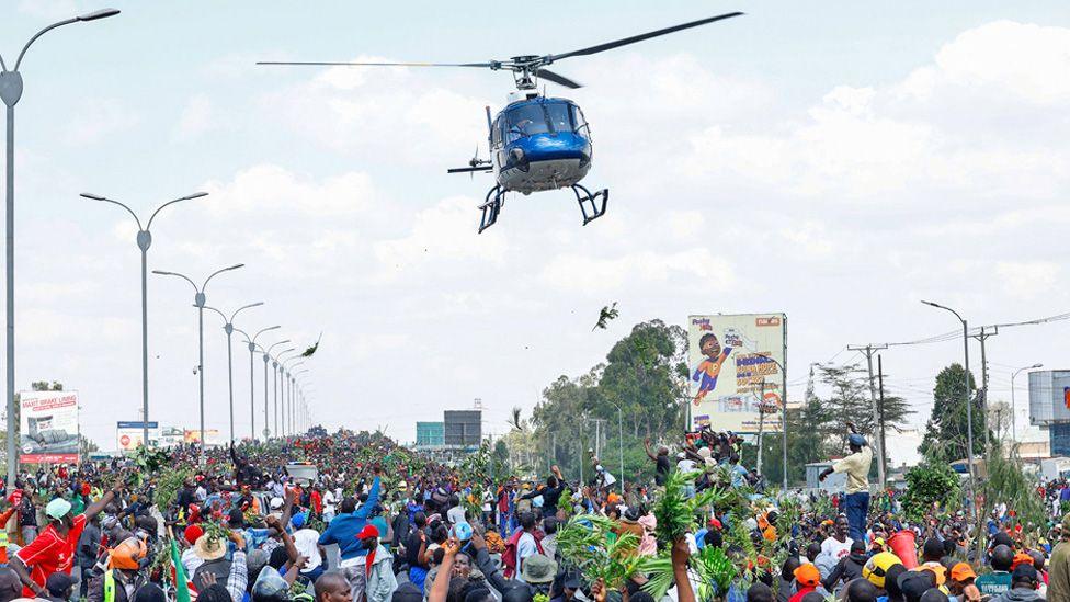 A helicopter flying over a mass of people - mourners of Raila Odinga - on a motorway in Kenya - 16 October 2025