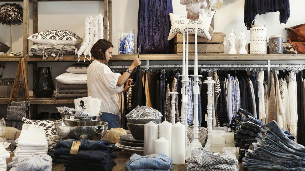 A shop assitant hangs up clothes in fashion store