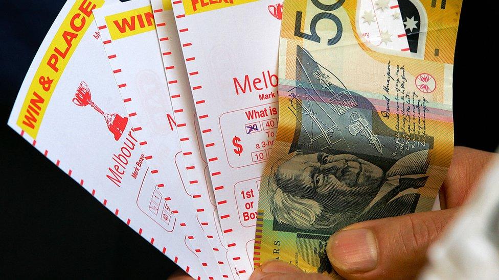 A person holds a A$50 note and gambling receipts