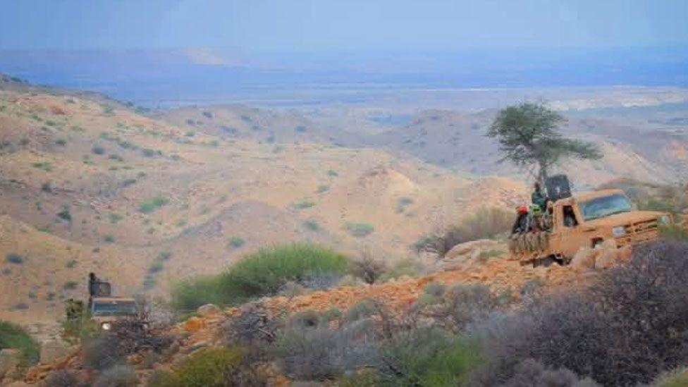 Several trucks carrying soldiers driving over rugged terrain in the mountains of Puntland