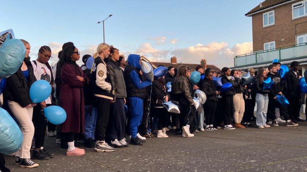 A line of people mainly in coats holding balloons - many of which are blue