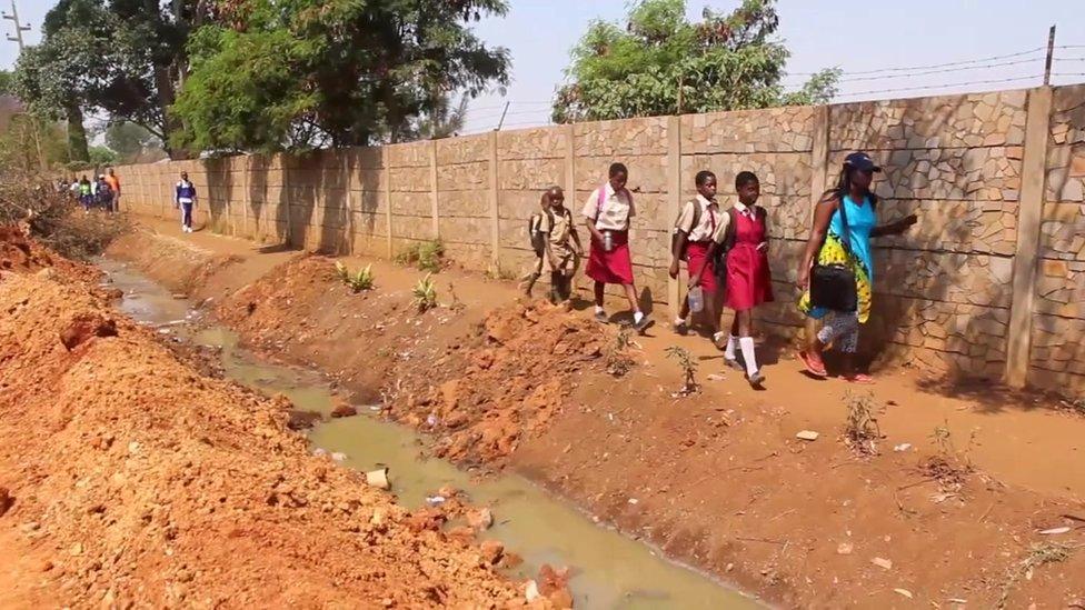 People walk next to an open drain