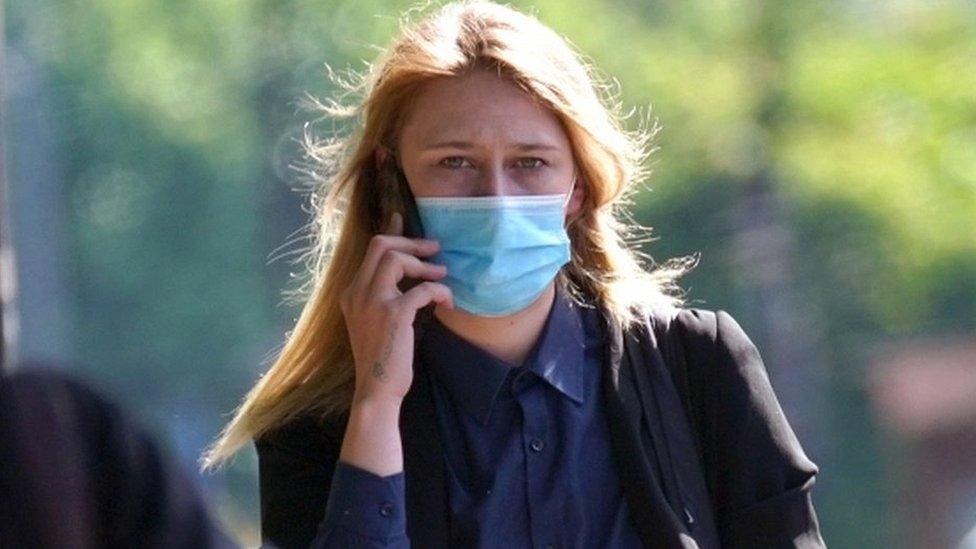 A head and shoulders shot of Lauren Saint George wearing a face mask and holding a phone to her ear.