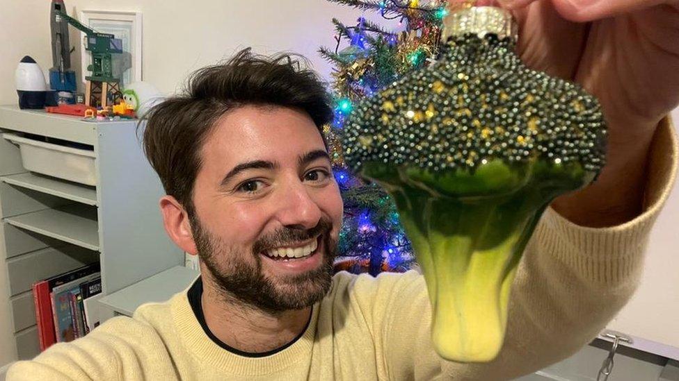 Ricky holding a broccoli ornament in front of his Christmas tree