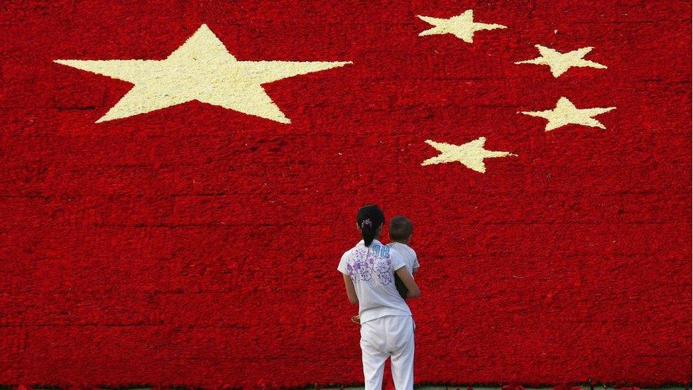 A woman holds her son as she looks at the national flag made up of 100,000 carnations at Wuling Square 25 September 2007 in Hangzhou, China.