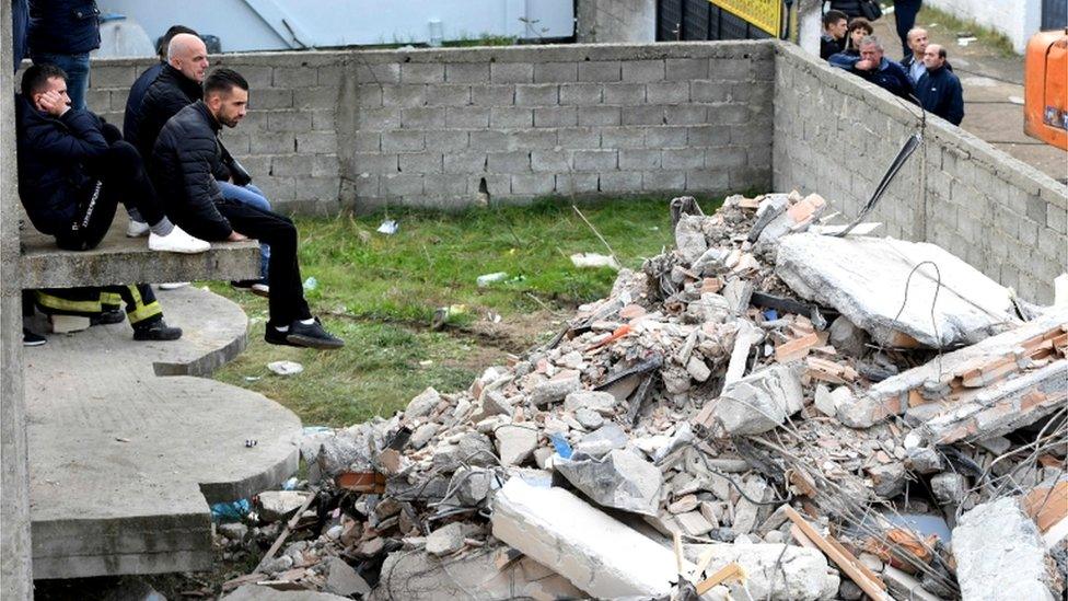 Onlookers watch as Italian rescuers search through the rubble of a collapsed building in Thumane, 27 November 2019