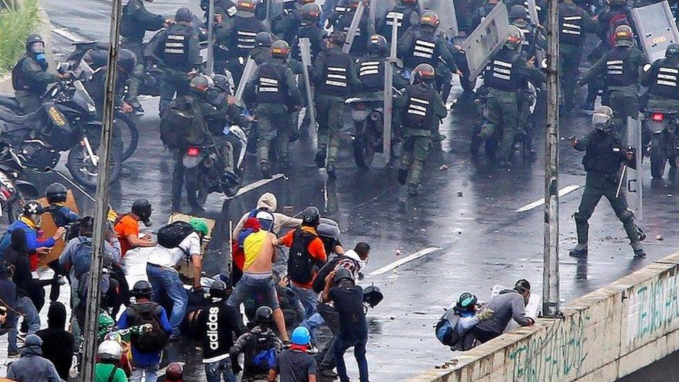 A member of the riot security forces points what appears to be a pistol towards a crowd of demonstrators during a rally