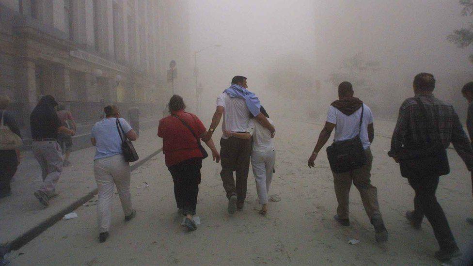 Ten men and women flee as one of the towers of the World Trade Center collapses in New York on 11 September, 2001. The pavement beneath their feet is covered with debris and the air is full of smoke.