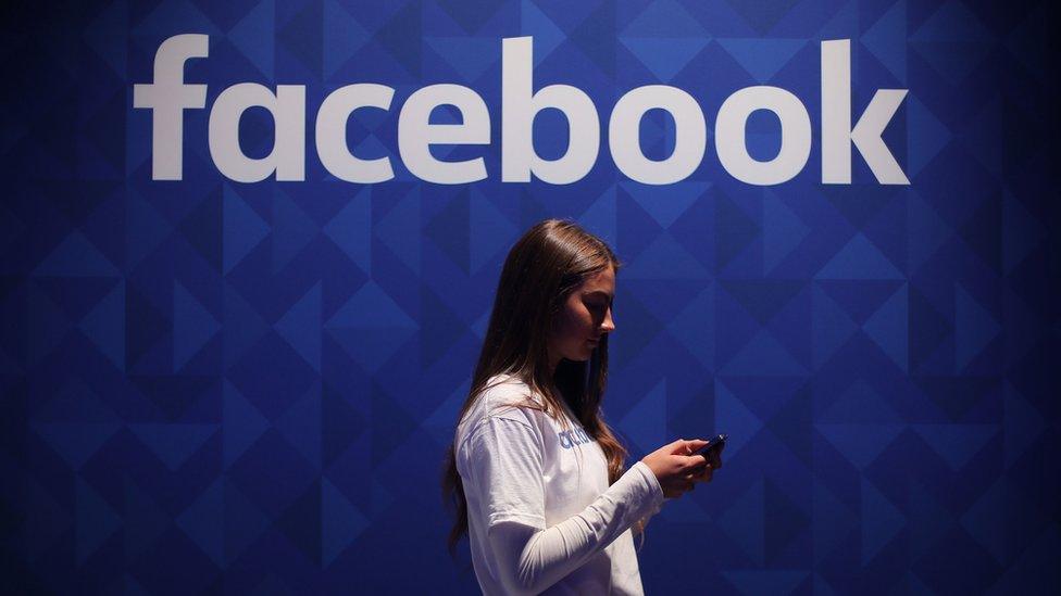 Woman uses her phone under a Facebook logo