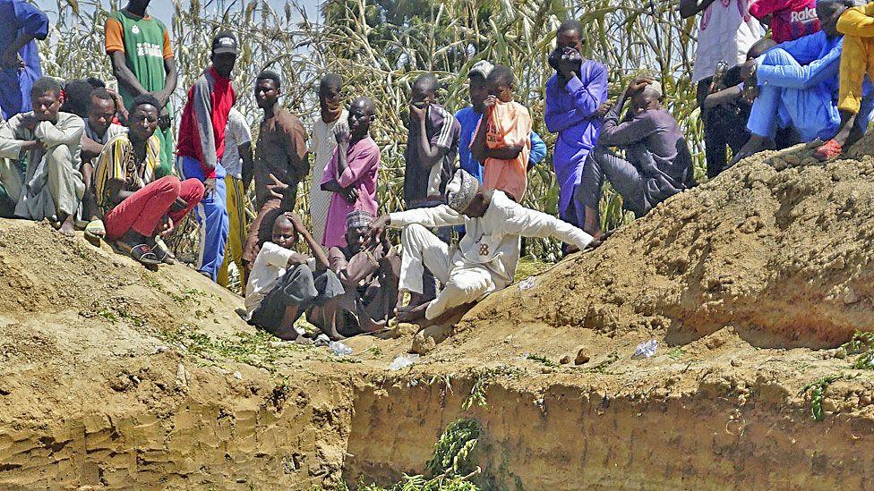 People sit by the side of a mass grave in Majia, Nigeria - 16 October 2024