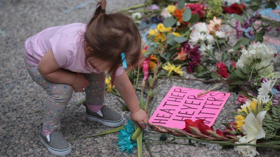 A young girl puts flowers on a memorial to Heather Heyer with a sign 'Heather Heyer matters'