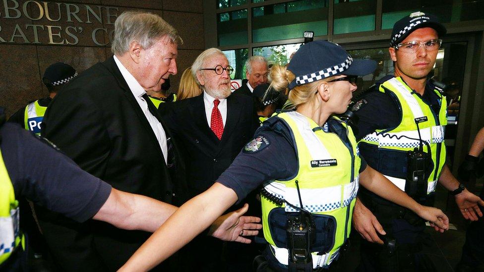 Cardinal George Pell and his lawyer Robert Richter are shielded by police upon entering court