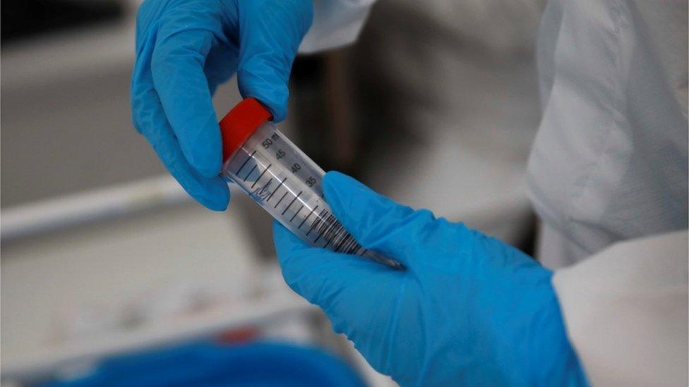 A woman wearing a protective coverall holds a test at a coronavirus disease (COVID-19) drive-thru testing centre