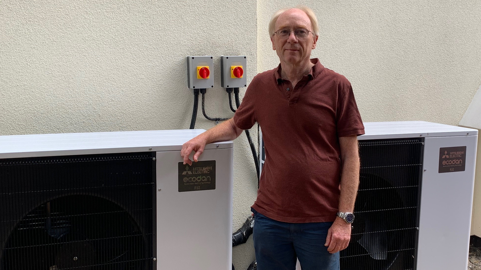 Dave Baldwin in T-shirt and shorts stands to the right of his heat pump