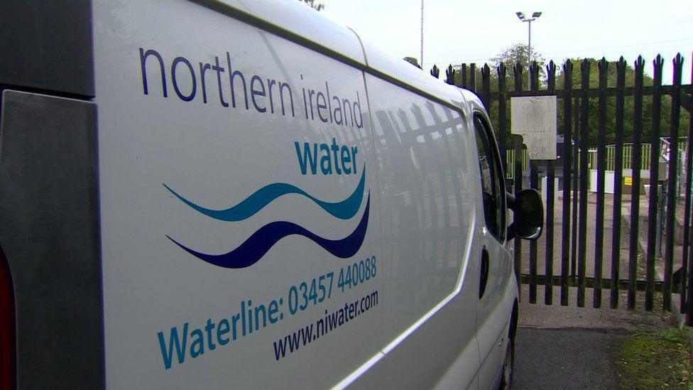 A white NI Water van parked up against a metal fence, on its side is the company's phone number and website address