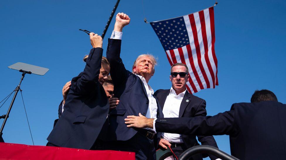 Republican presidential candidate former President Donald Trump gestures as he is surrounded by Secret Service agents as he leaves the stage at a campaign rally, in Butler, Pennsylvania