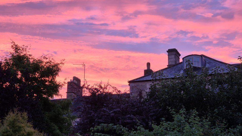 Sparse bright pink clouds over rooftops at dawn