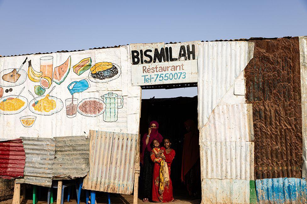 A woman and two children are seen standing in the doorway of a cafe in Garowe refugee camp