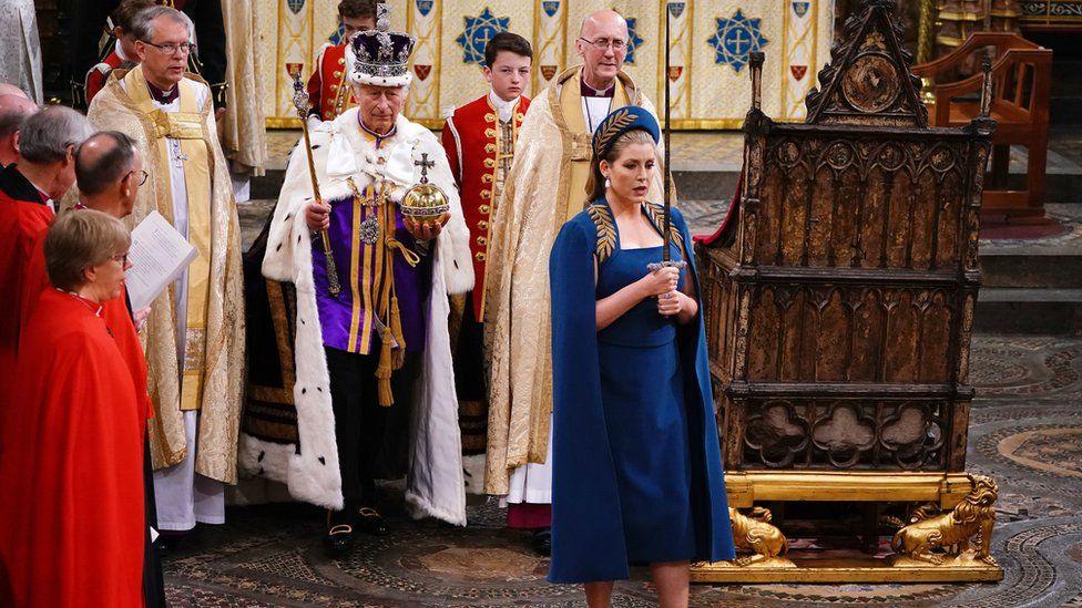 Dressed in blue, Penny Mordaunt carries the royal sword in front of King Charles III at the Coronation