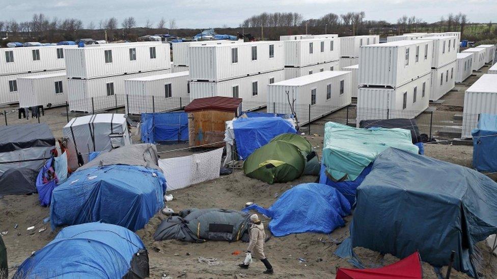 Migrant walks among tents in a makeshift camp as containers are put into place to house migrants living in the Jungle in Calais