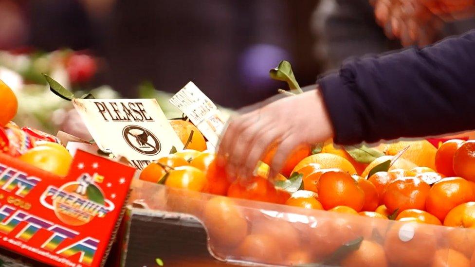 A hand touching oranges at a market