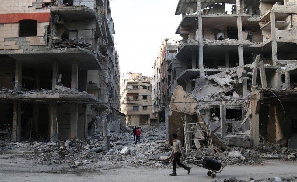 A Syrian youth pulls a cart past destroyed buildings in the town of Ayn Tarma, in the eastern Ghouta