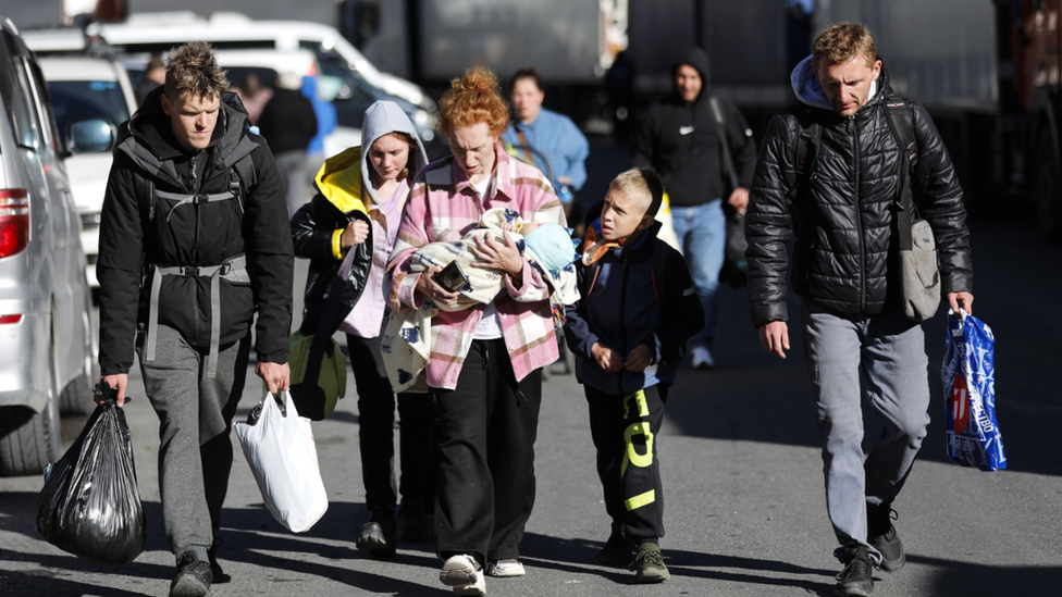 Young man, a woman with a baby and children walk to cross the border from Russia into Georgia. Photo: 27 September 2022