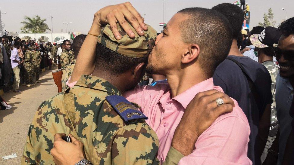 A Sudanese anti-regime protester kisses a soldier on the head during protests on April 11, 2019 in the area around the army headquarters in Sudan"s capital Khartoum