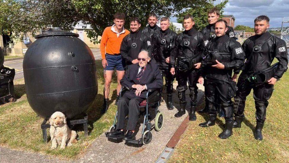 War veteran Boyd Salmon sits in a wheelchair at the Royal Navy's Portsmouth base surrounded by eight members of the navy's current diving team