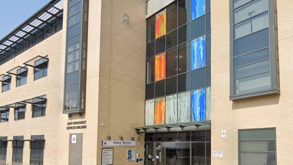 Cream brick building with numerous grey windows and coloured white, orange and blue glass above entrance doors